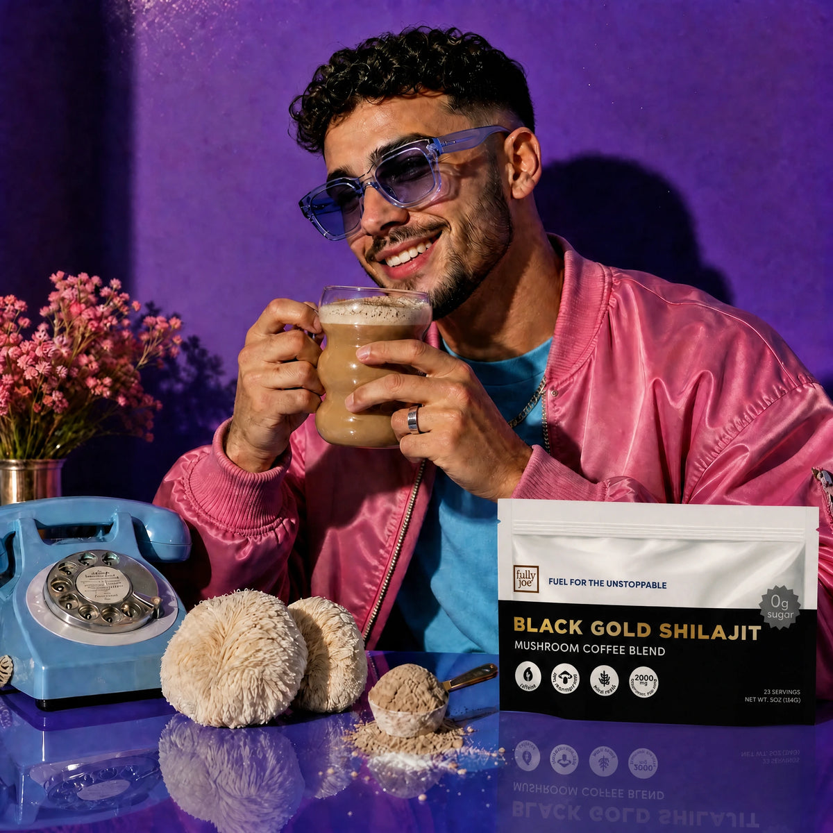 A man in sunglasses and a pink jacket drinks coffee beside a rotary phone, flowers, and a packet labeled "Fully Nutrition Shilajit Coffee" by Fully Nutrition, set against a purple background.
