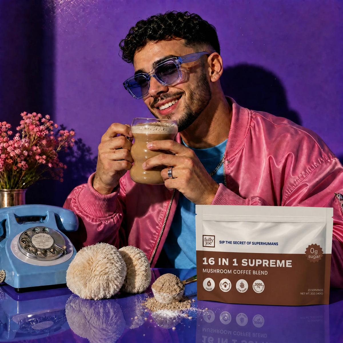 A man in a pink jacket and blue sunglasses holds a mug of coffee next to a bag of Fully Nutrition 16 in 1 Mushroom Blend Coffee from Fully Nutrition, accompanied by a blue rotary phone, flowers, and mushroom decor on a purple background.